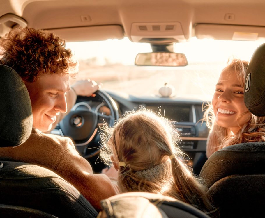 Family road trip with smiles under sunlight, enjoying a scenic drive together in the car.