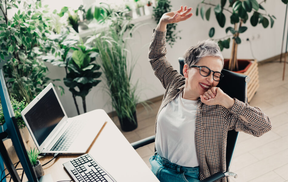 Person joyfully stretching in home office surrounded by lush indoor plants.
